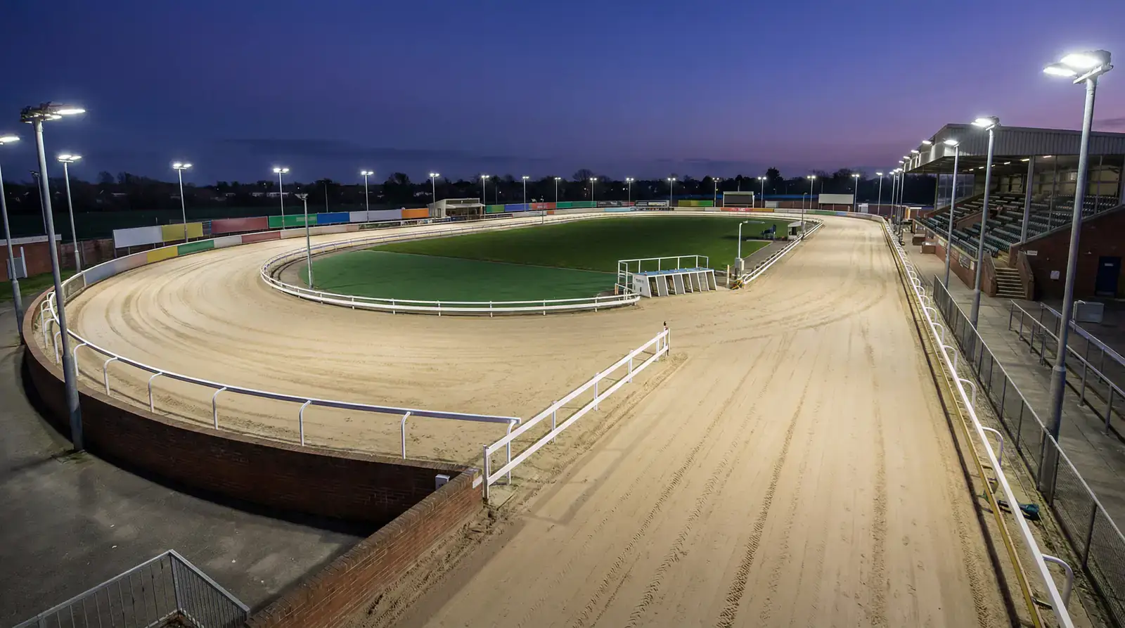Evening greyhound racing at Romford stadium under floodlights with dogs approaching the first bend